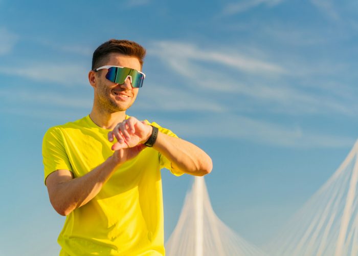 Uses a fitness watch, workout warm-up fitness man in sports glasses smiling.